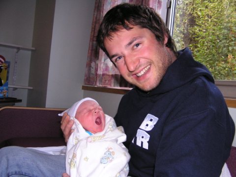 [Photo: Adam smiles poudly holding a yawning newborn Max]